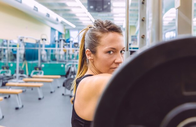 Photo portrait of woman lifting barbell in gym