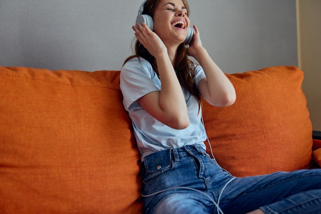 Portrait of a woman listening to music with headphones on the orange sofa unaltered