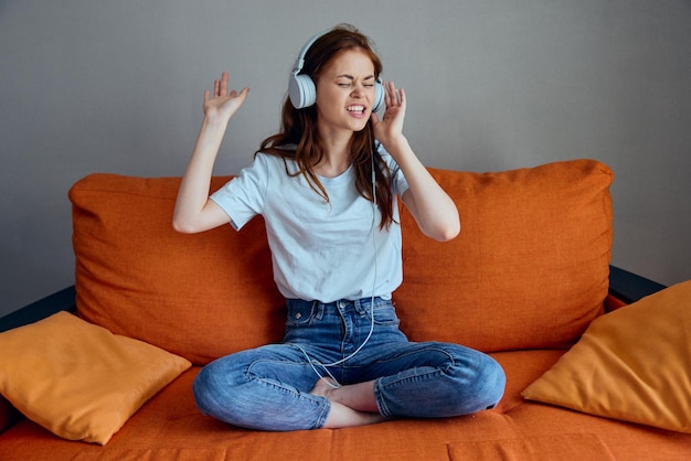 Photo portrait of a woman sitting on the couch at home listening to music on headphones lifestyle high quality photo