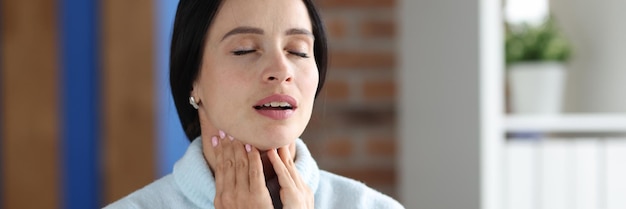 Portrait of woman sitting with closed eyes and sore throat on sofa painful symptoms in throat