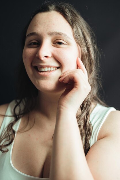 Portrait of a woman smiling and holding her hand to her face posing in a studio with black background Young adult applies daily care nourishing facial mask on her skin