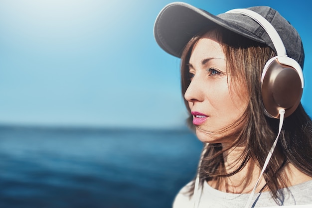 portrait of a woman in sunglasses wearing a cap who enjoys music on the background of the sea.