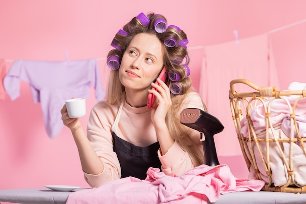 Portrait of a woman talking on the phone while sipping coffee against a pink background