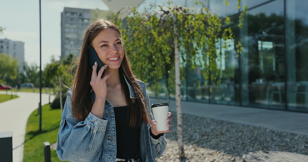 Portrait of woman walking with mobile phone and coffee cup Beautiful woman talking phone with takeaway coffee in hands on street