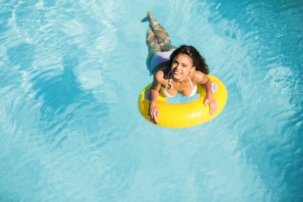 Portrait of woman in white bikini floating on inflatable tube in swimming pool