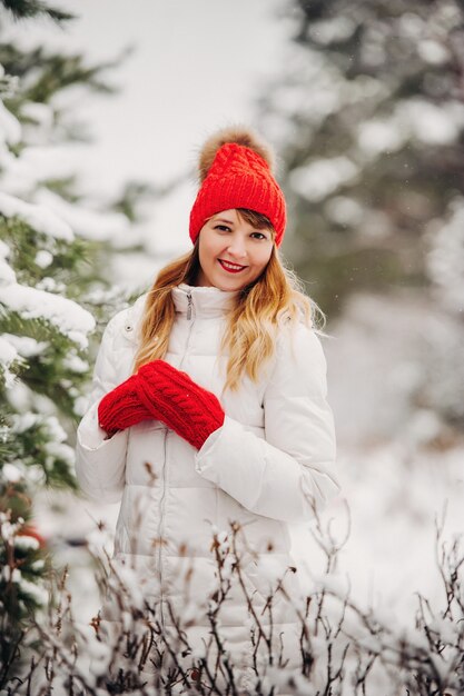 Portrait of a woman in white clothes and a red hat in a cold winter forest. Girl in a snow-covered winter forest