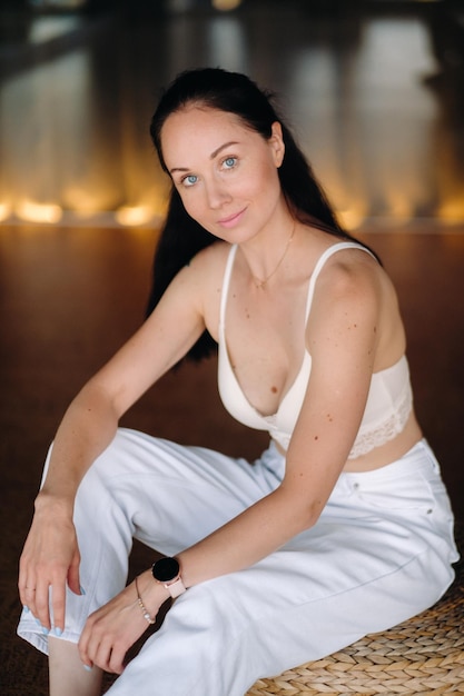 Portrait of a woman in white clothes sitting on an ottoman in the interior