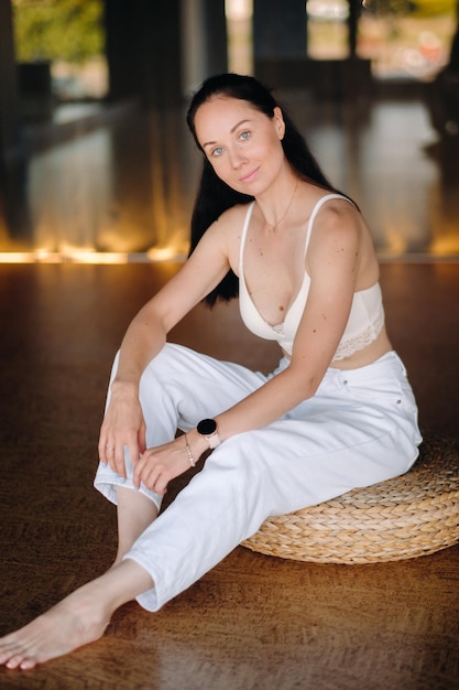 Portrait of a woman in white clothes sitting on an ottoman in the interior