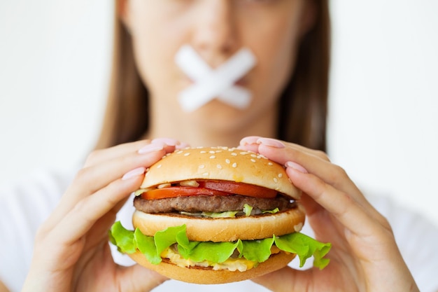 Portrait of a woman who wants to eat a burger but her mouth is taped