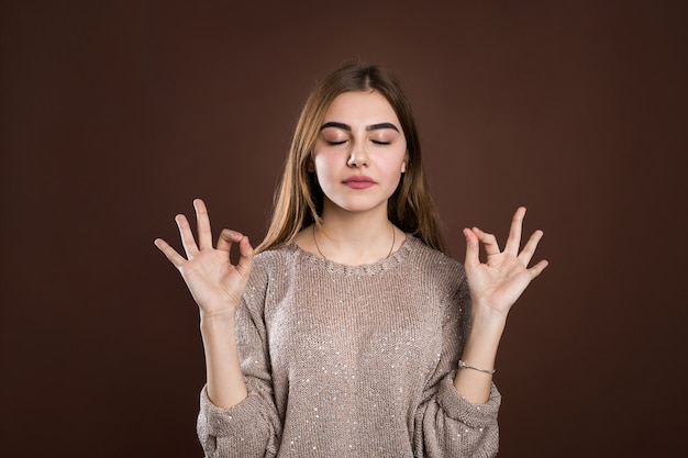 Portrait woman with calm and relaxed expression, standing in yoga pose with spreaded arms and zen signs over brown wall. Girl feels relieved after morning meditation