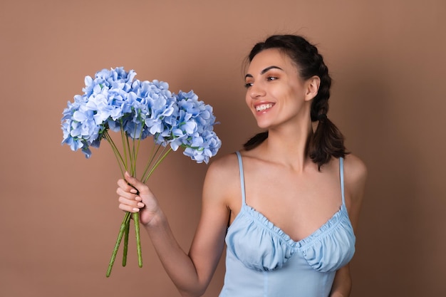 Portrait of a woman with perfect skin and natural makeup on a beige background with pigtails in a dress holding a bouquet of blue flowers