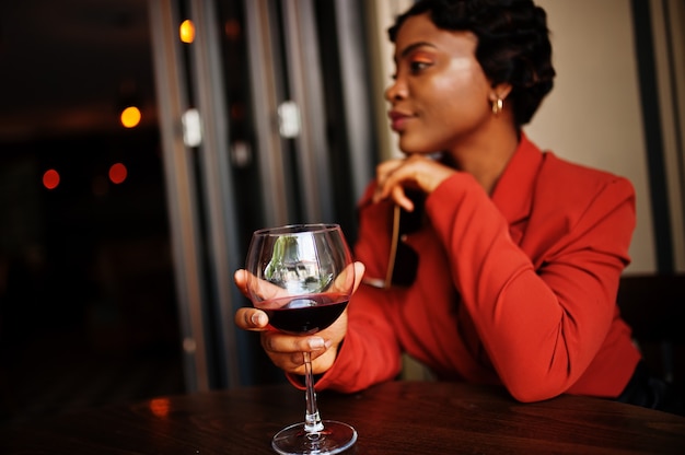 Portrait of woman with retro hairstyle wears orange jacket at restaurant with glass of wine