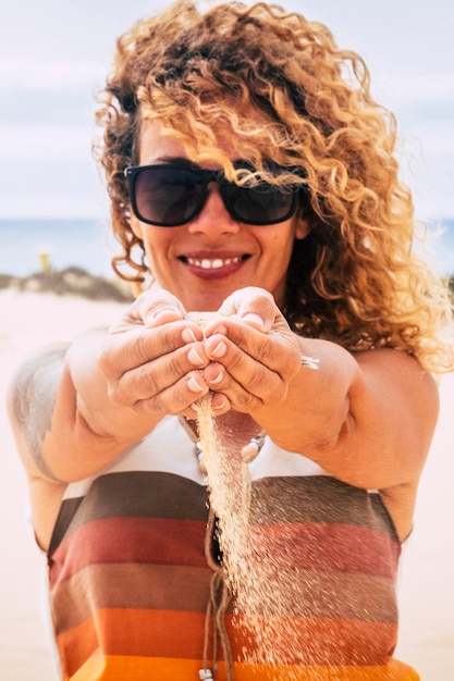 Portrait of woman with sand waterfall from hands summer style holiday vacation outdoor concept happy female enjoy sun and freedom with beach and ocean in background