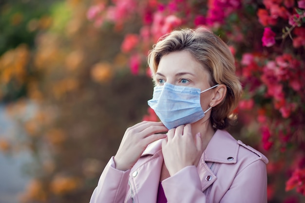 A portrait of woman with short blond hair with medical face mask outdoor. People, healthcare and medicine concept.