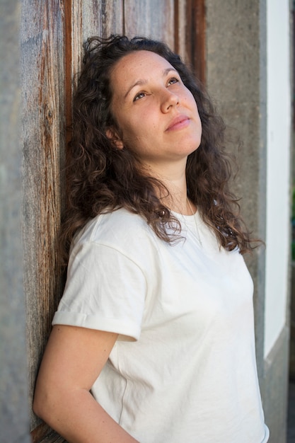 Portrait of woman with a white blouse, with curly hair, brunette and looking up.