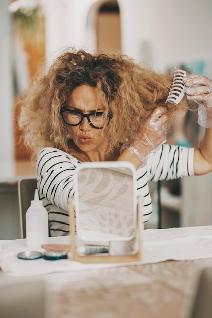 Portrait of woman with worried expression changing hair colours at home from herself Hair style diy concept work Female with long hair in colouring operation indoor Young lady beauty care time