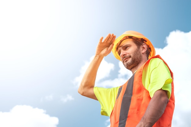 A portrait of a worker stands with confidence in an orange work suit and safety helmet against the sky Smart industrial worker work concept