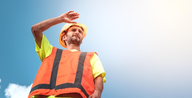 A portrait of a worker stands with confidence in an orange work suit and safety helmet against the sky Smart industrial worker work concept