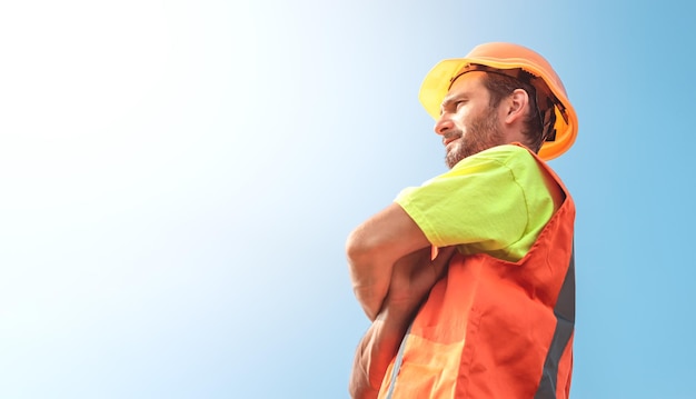 A portrait of a worker stands with confidence in an orange work suit and safety helmet against the sky Smart industrial worker work concept