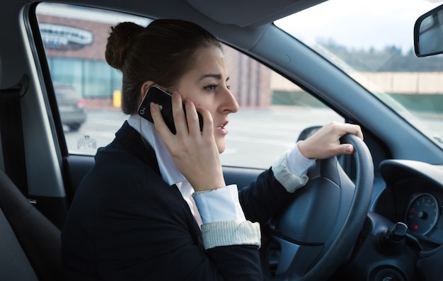 Portrait of worried businesswoman driving car and talking by phone