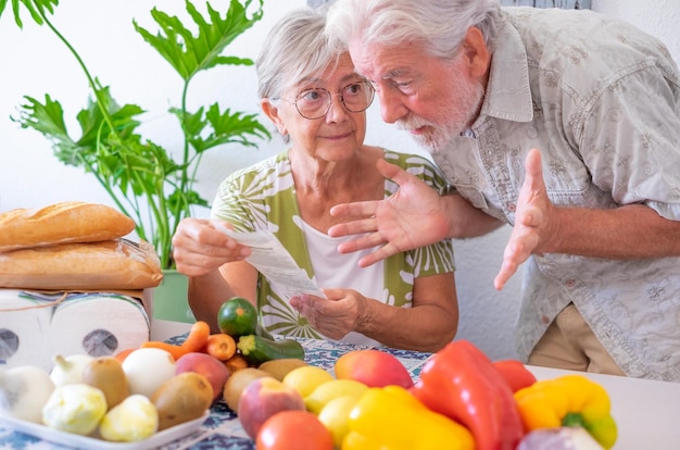 Portrait of worried old senior couple at home table holding grocery receipt discussing for rising prices Bankruptcy financial difficulties concept Human emotions expressions