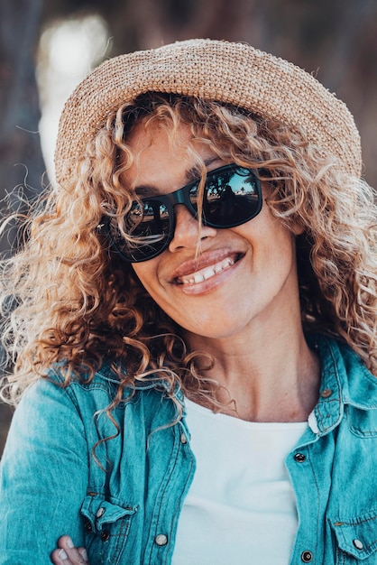 Portrait of young adult woman smiling at the camera with sunglasses and straw hat Female people happy in outdoors leisure activity Defocused background with road Copy space on the right