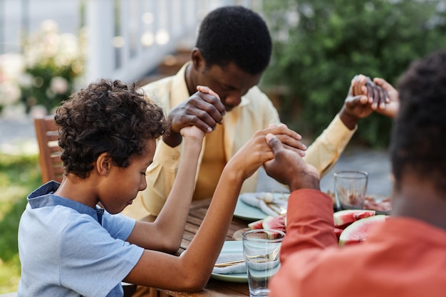 Portrait of young african american boy saying grace at table outdoors during family gathering and ho