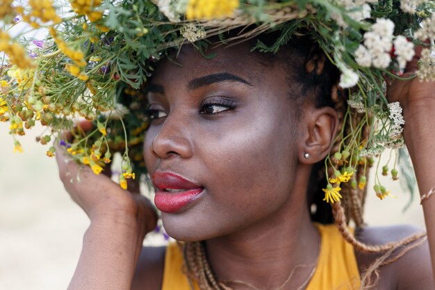 Portrait of a young African American female , model of fashion, with big flowers in her hair. Portrait of a girl in a crooked plan in a field with flowers. wreath on her head