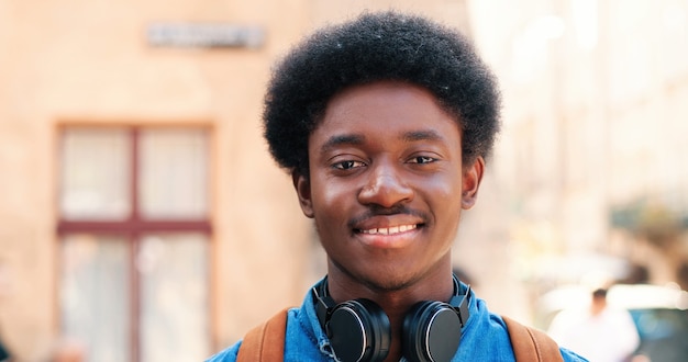 Portrait of young african american guy of multiracial ethnicity with headphones standing on the warm...