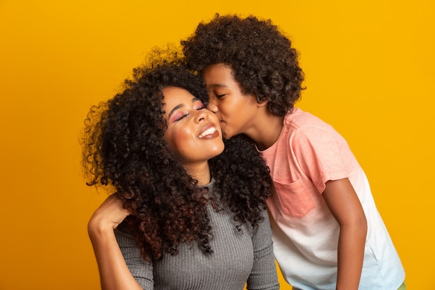 Portrait of young African American mother with toddler son. Son kissing his mother. yellow wall. Brazilian family.