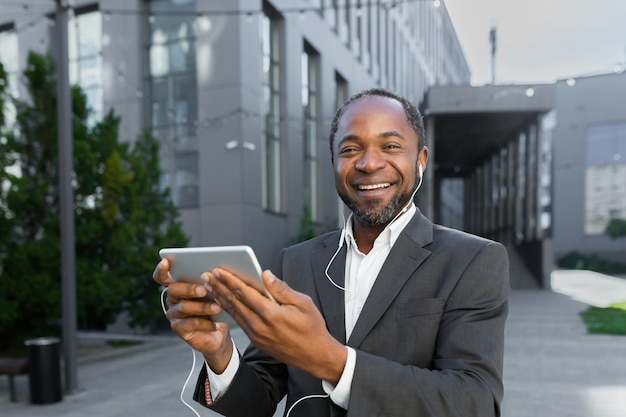 Portrait of young african american student in suit standing near campus wearing headphones he holds