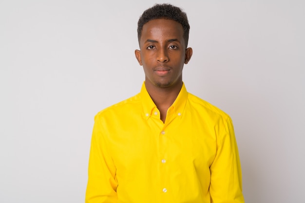 Portrait of young African businessman with Afro hair wearing yellow shirt against white wall