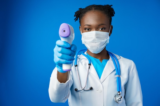 Portrait of young african female doctor in medical mask in blue studio