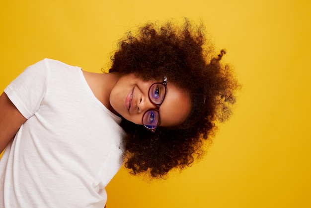 Portrait of a young African girl in glasses smiling and rejoicing on a clean yellow background