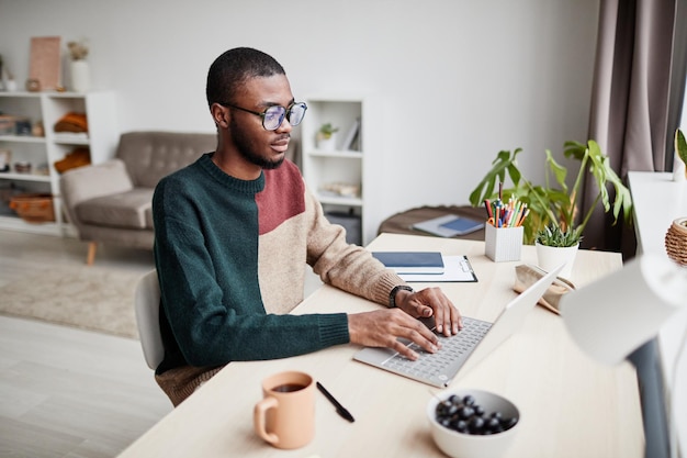 Portrait of young africanamerican man wearing glasses while working from home and using laptop copy ...