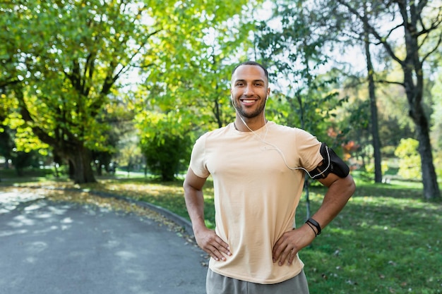 Portrait of a young africanamerican sportsman standing in a park in a sports uniform and headphones