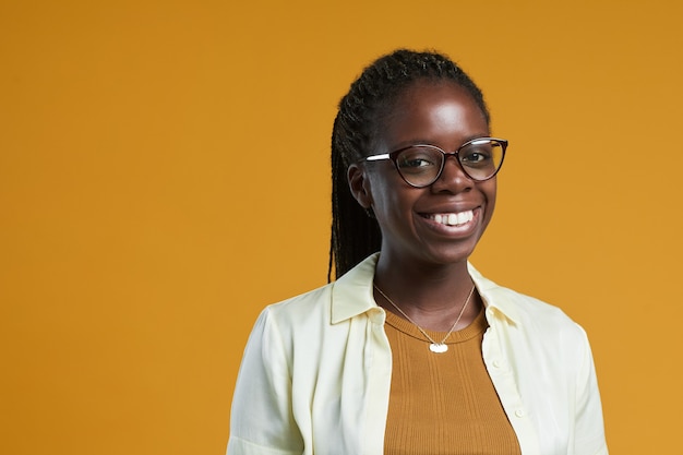 Portrait of young africanamerican woman wearing glasses and smiling at camera while posing against y...