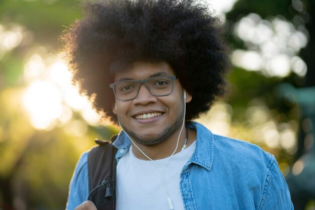 Portrait of young afro latin man listening music with earphones while walking outdoors on the street. Urban concept.