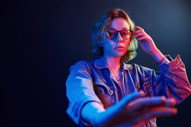 Portrait of young alternative girl in glasses with green hair in red and blue neon light in studio