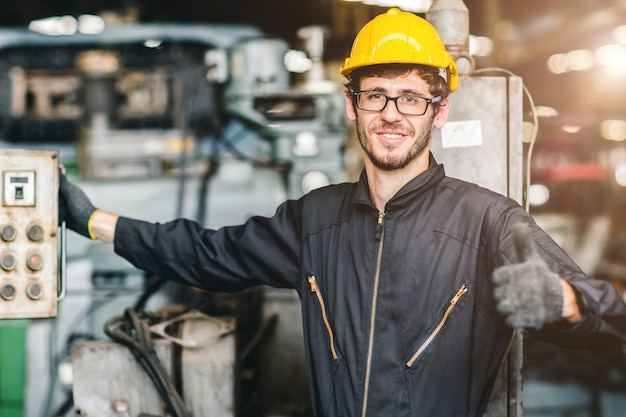 Portrait of young American happy worker enjoy happy smiling to work in a heavy industrial factory.Thumb up with machine controller.