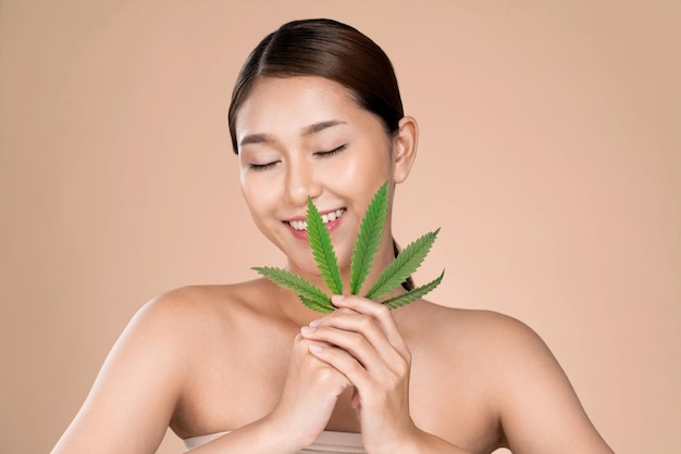 Portrait of young ardent girl with healthy fresh skin holding green hemp leaf