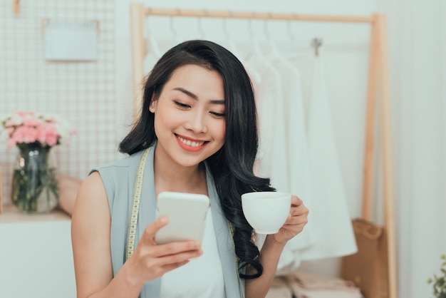 Portrait of young Asian business woman/fashion designer take a rest while drinking coffee and using mobile phone