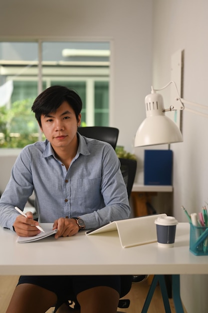 Portrait of young asian businessman sitting at home office and looking at camera