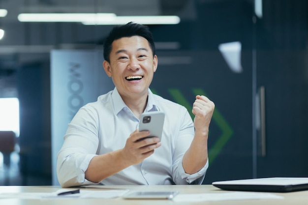 Portrait of a young asian businessman sitting in the office and holding the phone received a message