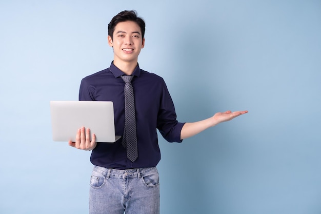 Portrait of young Asian businessman using laptop on blue background