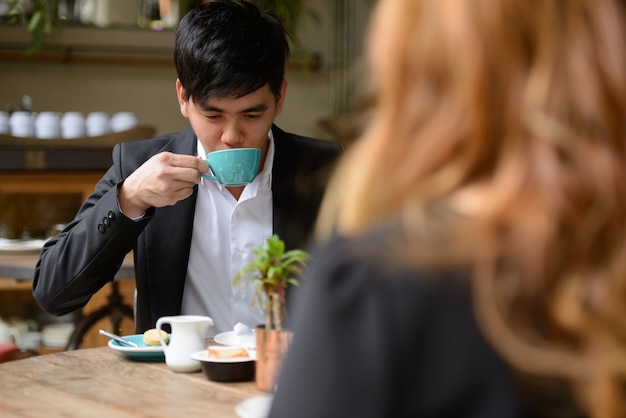 Portrait of young Asian businessman and young Asian businesswoman together relaxing at the coffee shop