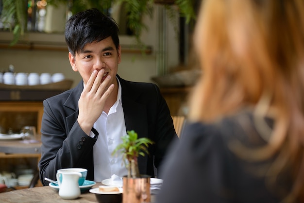 Portrait of young Asian businessman and young Asian businesswoman together relaxing at the coffee shop