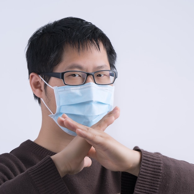 Portrait of young Asian man, saying no to coronavirus infection with wearing medical surgical blue face mask isolated on white background, close up, closeup.