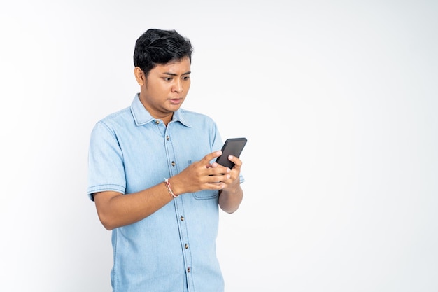 Portrait of young asian man shocked watching video using cell phone on isolated background