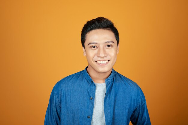 Portrait of young Asian man smiling isolated on orange background